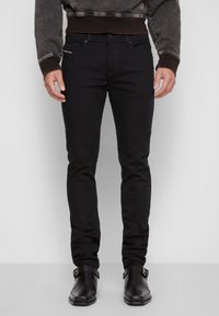 Jeans de mezclilla negra con un ajuste slim, que presentan un cierre de botón, cinco bolsillos y una marca sutil en la parte frontal. Tejido texturizado.
