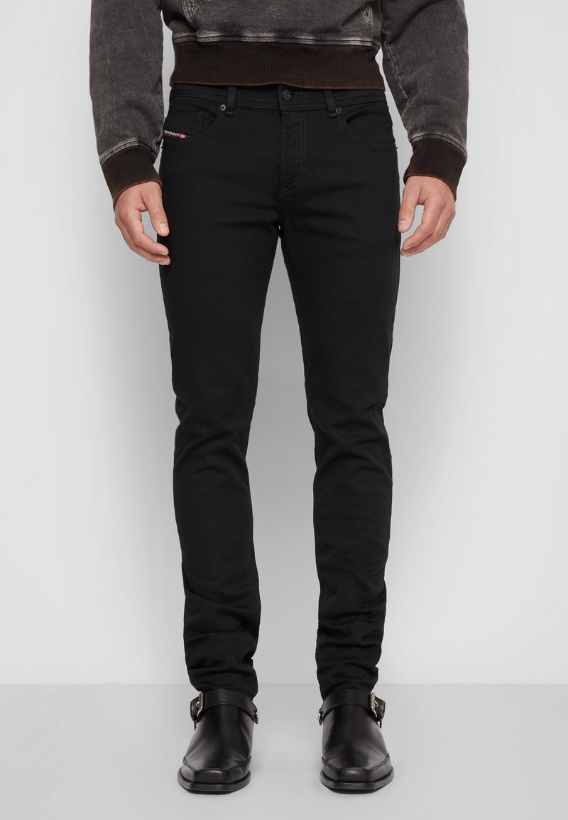 Jeans de mezclilla negra con un ajuste slim, que presentan un cierre de botón, cinco bolsillos y una marca sutil en la parte frontal. Tejido texturizado.