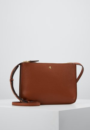 Bruine leren crossbodytas met gouden rits en klein gouden logo aan de voorkant, tentoongesteld op een wit voetstuk tegen een effen achtergrond.