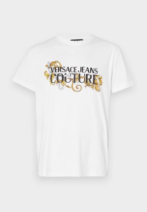 T-shirt bianco in cotone con testo grafico nero e oro "VERSACE JEANS COUTURE" con accenti floreali decorativi. Maniche corte e colletto tondo.