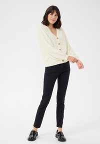 Cream cable-knit cardigan with a V-neck, featuring large buttons and puffed sleeves, paired with black slim-fit pants and shiny black loafers.