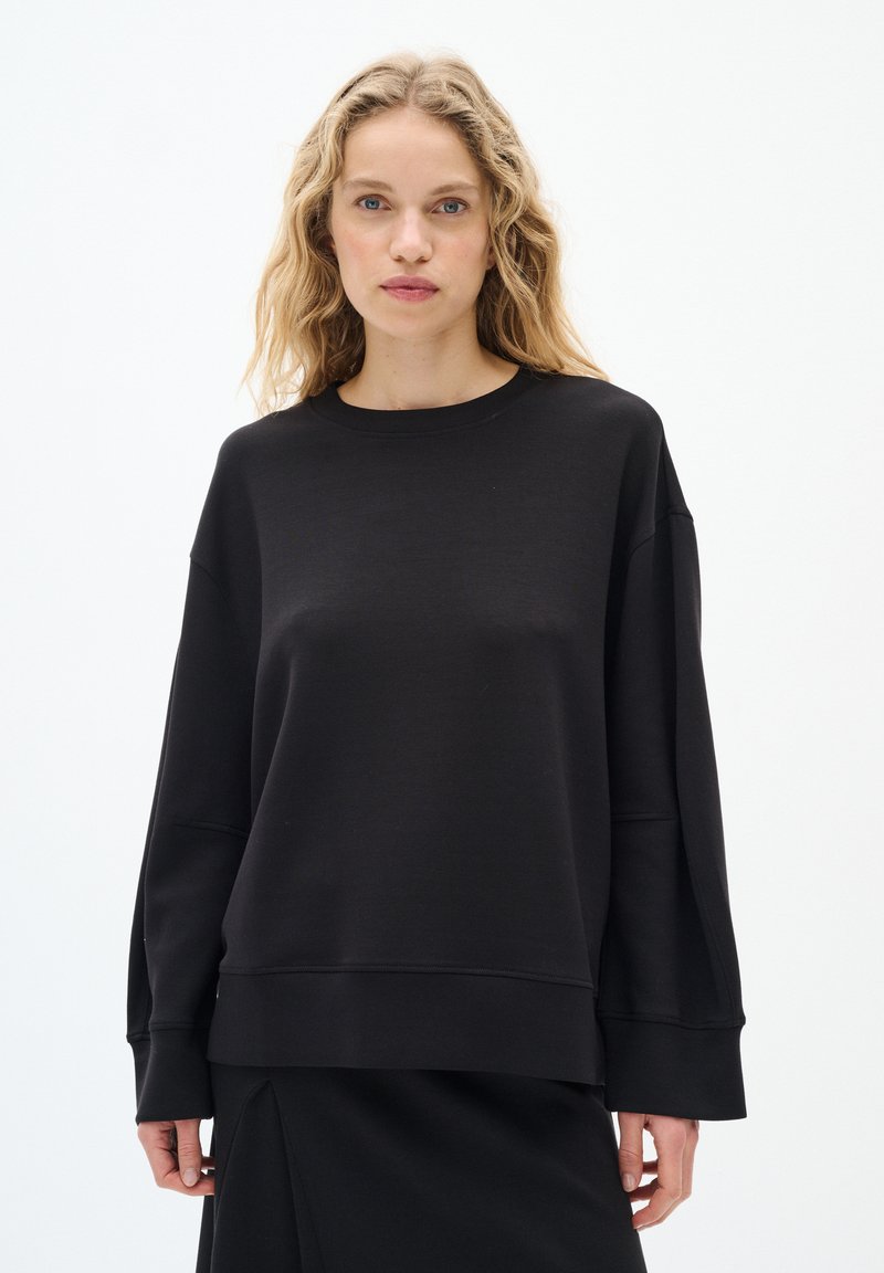 Felpa nera oversize con scollo rotondo, spalle scese e polsini a coste. Realizzata in tessuto liscio con una vestibilità comoda.