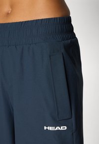 Jūras spēku aktīvās šortus, izgatavotas no gludas auduma, ar elastīgu jostu, sānu kabatu un baltu logotipa detaļu apakšmalā.