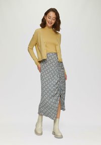 Gelb gestreifter Rollkragenpullover, kombiniert mit einem midi Rock im floralen Muster mit Raffung und einem Seitenschlitz. Beige Ankle Boots runden den Look ab.