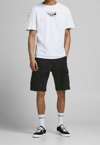 Bílý bavlněný tričko s potiskem "Beach Club"; černé cargo šortky s kapsami; bílé ponožky; černé tenisky. Jednoduchý, neformální outfit.
