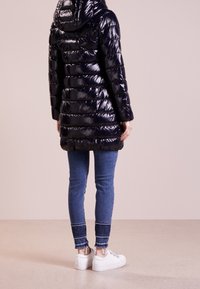 Blank pufferjacka i svart med huva, med kviltade ränder och långa ärmar, parat med blå jeans och vita sneakers.