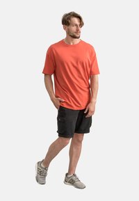T-shirt en coton corail à manches courtes pour homme avec un col rond, associé à un short cargo noir avec deux poches latérales, et des baskets grises.