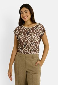 Top marrón con estampado y acentos en crema, de manga corta y corte relajado, combinado con pantalones beige de talle alto con bolsillos laterales.