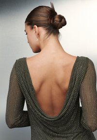 Rochie verde măslinie cu spatele jos, mâneci lungi din material transparent decorate cu mici cristale argintii, material neted care se drapează elegant pe spate.