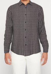 Schwarz-weiß kariertes Langarmhemd mit Knopfverschluss und halbtailliertem Schnitt aus strukturiertem Stoff.