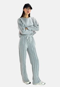Felpa grigia e pantaloni abbinati con strisce verticali, realizzati in materiale morbido. Comprende una cintura con cordoncino e un cappellino nero.