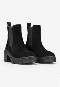 Botines de ante negros con paneles laterales elásticos, puntera cuadrada y tacón de goma grueso. Presenta una suela texturizada para mayor agarre.