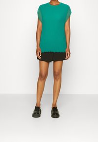 Teal ribbet top med korte ærmer og en rund halsudskæring, parret med en sort plisseret nederdel og sorte loafers. Glat tekstur, afslappet design.