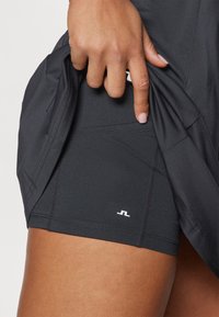 Svarta atletiska shorts i ett töjbart material, med en sidoficka och en liten vit logotyp vid fållen. Slät och figurnära design.