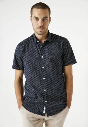 Camisa de manga corta abotonada en azul marino con un estampado dorado ondulado, con un cuello estándar y botones blancos. Tejido texturizado, corte casual.