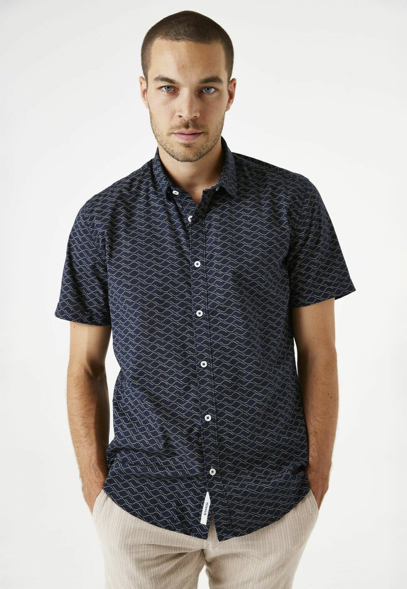 Chemise à manches courtes avec boutons en bleu marine, ornée d'un motif doré en ondulation, dotée d'un col standard et de boutons blancs. Tissu texturé, coupe décontractée.