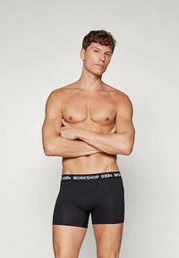 Melnas bokseru bikses ar baltu logotipa joslu, izgatavotas no gludas auduma. Dizains ir pieguļošs un minimālistisks, bez papildu rakstiem.