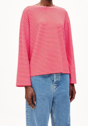 Personne portant un haut à manches longues rayé horizontalement rouge et blanc et un jean bleu taille haute sur fond blanc.