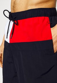 Shorts da nuoto blu navy con bloccaggio dei colori orizzontale in rosso e bianco. Presentano una vita elastica con cordino e tasche laterali. Texture liscia.