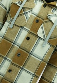 Bruine en beige flanellen shirt met een geruit patroon, twee borstzakken, grijze koord en zwarte knopen op een zachte, gestructureerde stof.