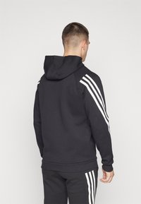 Felpa nera con cappuccio e design a tre strisce bianche sulle spalle e sulle maniche. Realizzata in tessuto morbido con una vestibilità comoda.