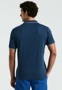 Polo shirt bleu marine à manches courtes, avec des bordures blanches au niveau du col et des manches, présentant une texture de tissu lisse.