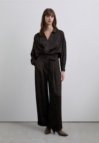 Donkere, met patroon bedrukte jumpsuit met een V-hals, lange, losse mouwen, een ceintuur in de taille en brede pijpen, gecombineerd met beige hakken.