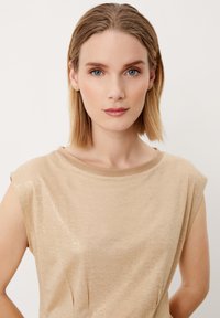 Beige mouwloos topje met een subtiele glans, geribbelde halslijn en zachte textuur. Bevat plooien aan de voorkant voor een ontwerpdetail.
