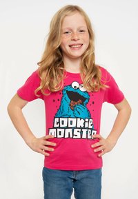 Pink cotton t-shirt featuring Cookie Monster graphic with oversized eyes and cookie, paired with blue denim jeans.