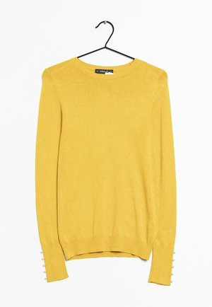 Pull en maille jaune avec des manches longues, un col rond, des fentes latérales et de petits boutons décoratifs blancs sur les poignets. Texture lisse.