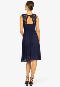 Marineblaue Robe mit Spitzenakzenten an den Schultern und einem plissierten Rock. Sie verfügt über ein tailliertes, gerafftes Oberteil und ein Schlüsselrücken-Design.