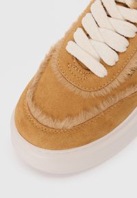 Baskets en daim tan avec des accents en fausse fourrure, lacets blancs et semelle extérieure texturée crème. Forme arrondie avec des détails de couture le long des bords.