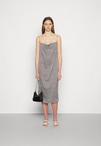 Vestido camisola com padrão de bolinhas em preto e branco, apresentando alças finas e uma fenda até a coxa. Combinado com sandálias brancas de tiras.