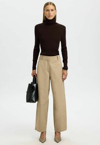 Rjav rebrast dungaree, bež široke hlače in bež špicaste pete. Črna torba z ukrivljenim ročajem. Gladke teksture, sodoben dizajn.