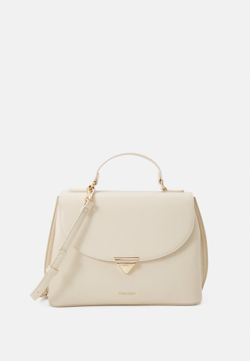 Sac à main structuré couleur crème avec poignée supérieure, bandoulière ajustable et fermoir triangulaire doré sur le rabat avant.