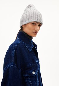 Grijze geribbelde gebreide beanie met een klep, gedragen bij een blauwe corduroy jas met grote zakken en een spitse kraag.