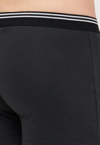 Schwarze Shorts aus glattem Stoff, mit einem schwarzen Bund mit weißen Streifen und einer taillierten Passform. Keine sichtbaren Muster oder Beschläge.