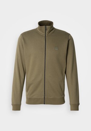 Veste zippée vert olive en tissu doux avec un col montant, des poignets côtelés et une petite étiquette logo sur la poitrine gauche.