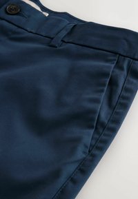 Tengerészkék nadrág gombos záródással, övbújtatókkal és oldalsó első zsebekkel, fehér felületen laposan elhelyezve.