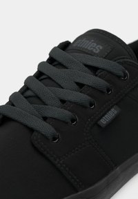 Μαύρα παπούτσια skate με υφή στην επάνω πλευρά, επίπεδες σκούρες γκρι κορδόνια και διακριτική λεπτομέρεια με branding. Ελαστική σόλα με ενισχυμένα ράμματα.