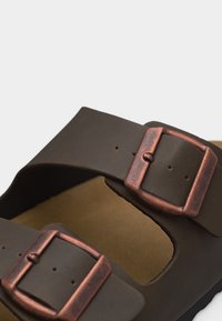 Sandale marron avec deux brides réglables et boucles rectangulaires de couleur cuivre sur une semelle couleur cuir clair.