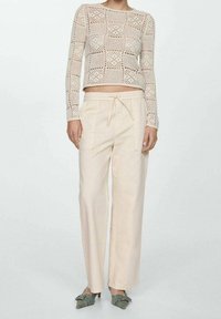 Světle béžový pletený top s dlouhým rukávem a čtvercovým vzorem, spárovaný s volně střiženými, světlé béžovými kalhotami s elastickým stažením v pase.