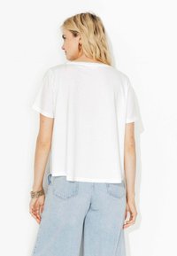 T-shirt blanc à manches courtes avec une coupe décontractée, texture douce et encolure arrondie. Associé à un jean large bleu clair.