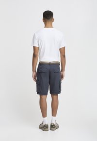 Laivaston raidalliset cargo shorts, joissa on taskut, yhdistettynä yksinkertaiseen valkoiseen t-paitaan ja lenkkareihin. Ominaisuuksiin kuuluu erottuva vyötärö ja käännettylahje.