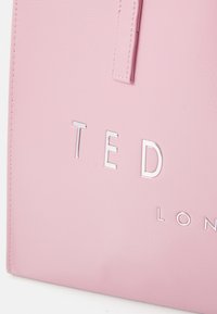Bolsa de tote em imitação de couro rosa, apresentando letras prateadas em relevo "TED" e "LONDON," com uma textura lisa e design minimalista.