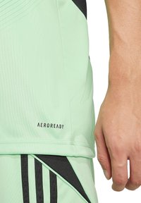 Helles mintgrünes Sportshirt mit tailliertem Schnitt, schwarzen Akzenten und dem "AEROREADY"-Logo nahe dem unteren Saum. Glattes, synthetisches Material.