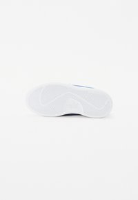 Semelle de chaussure avec une semelle extérieure texturée blanche arborant un motif en chevrons et des accents bleus près de l'arche. Logo imprimé sur la semelle.