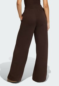 Hnedé tepláky s voľným strihom, elastickým pásom a bočnými vreckami. Mäkká látka a široké nohavice jemne sa zužujúce pri členku.