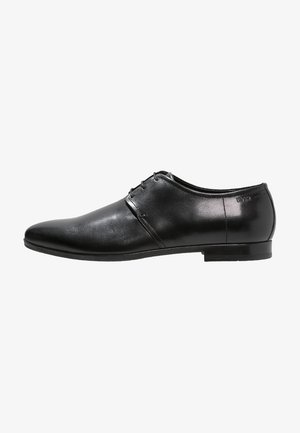 Chaussure habillée pour homme en cuir noir poli, avec bout pointu, fermeture à lacets et petit talon, vue de profil extérieur.