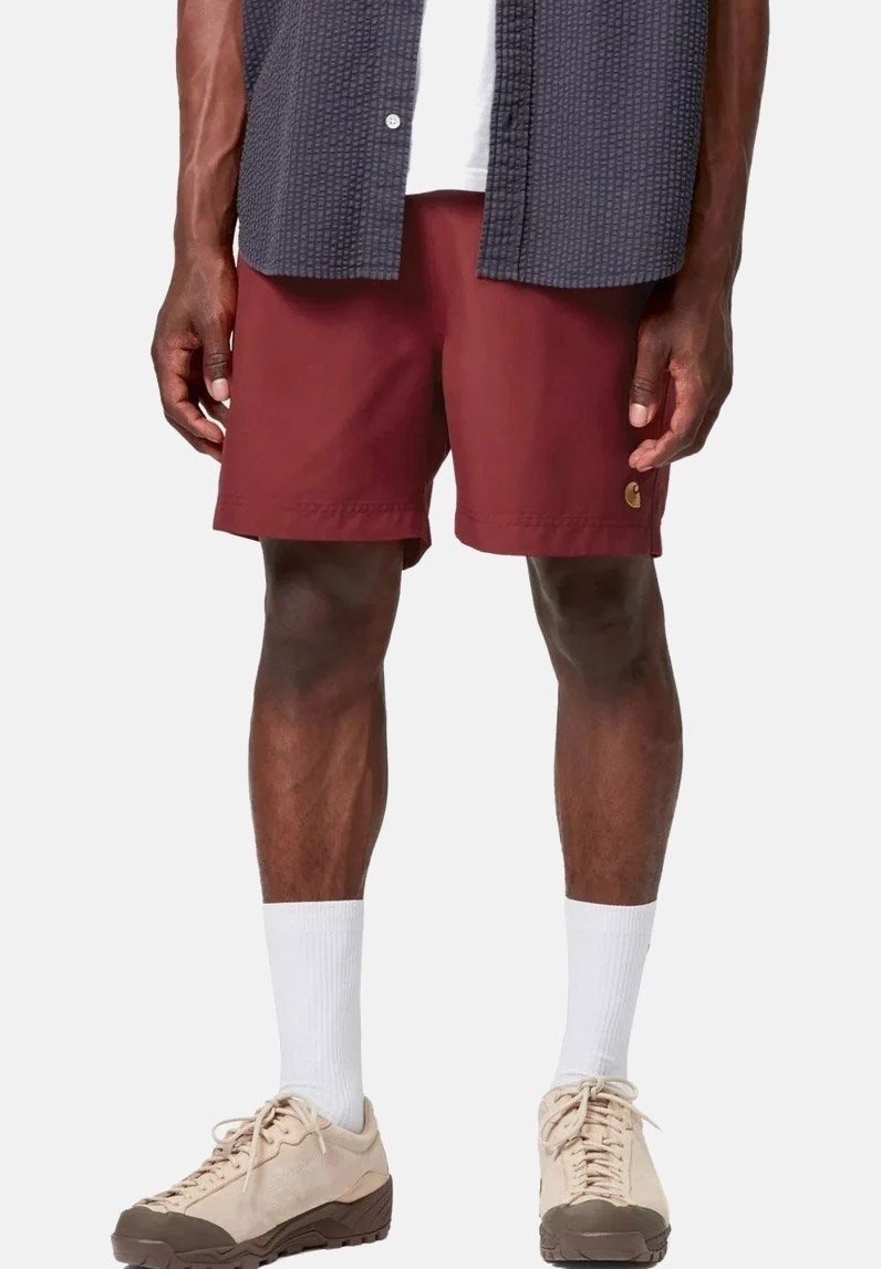 Mann trägt kastanienbraune Shorts, weiße Wadenstrümpfe, beige Turnschuhe und ein dunkel gemustertes Hemd über einem weißen T-Shirt.